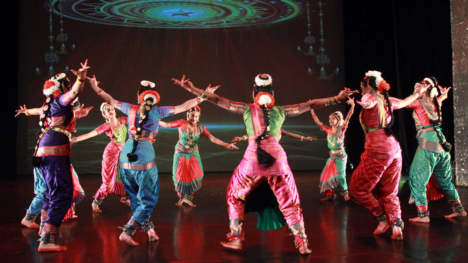 A group of young women in traditional Indian dress dancing on stage in a circle