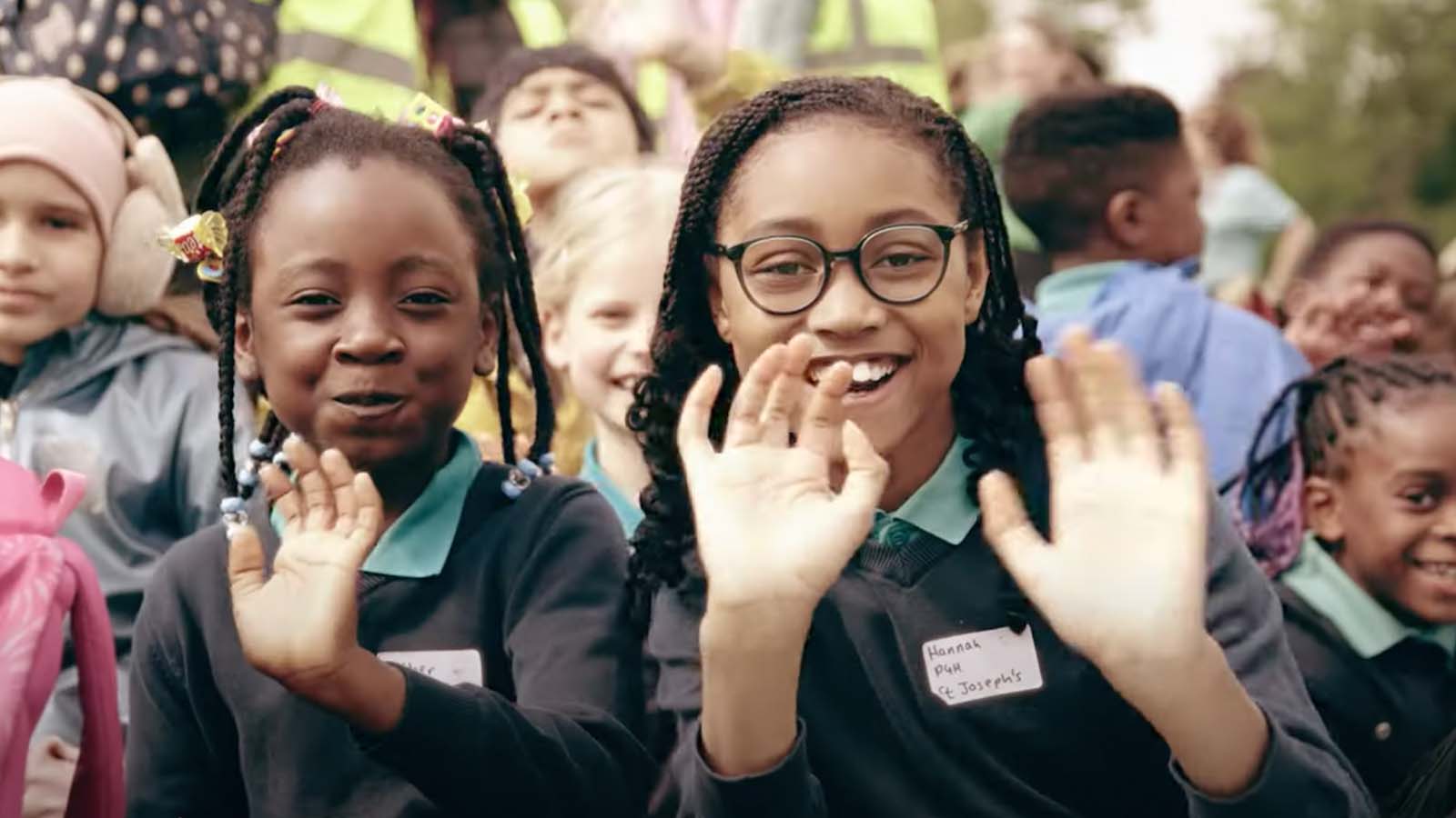 Two young primary school pupils waving in a crowd