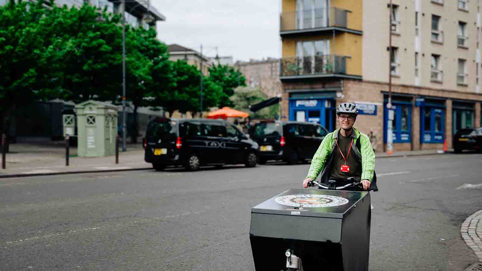 A man in a reflective jacket and helmet riding a cargo bike along a city street