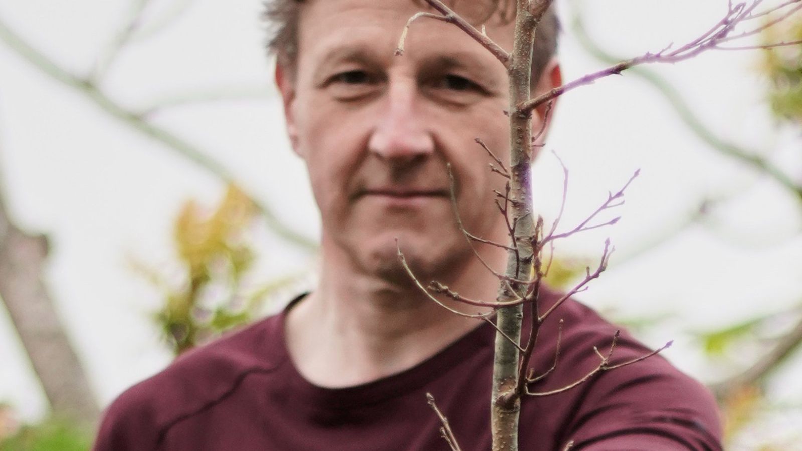 A man stands facing the camera holding a twig in his hand