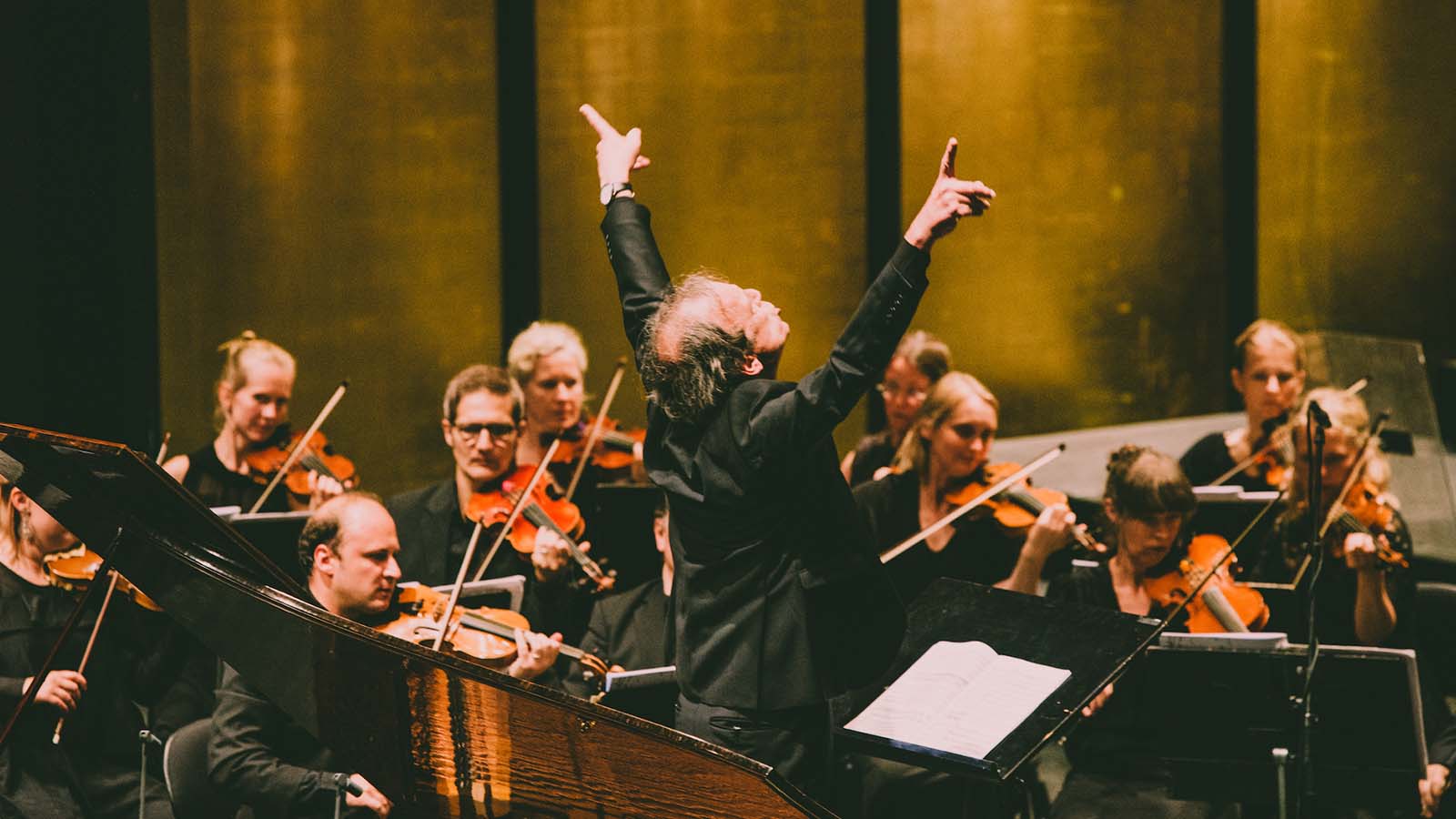 A man (Lars Ulrik Mortensen) gestures passionately with his hands in the air while conducting an orchestra
