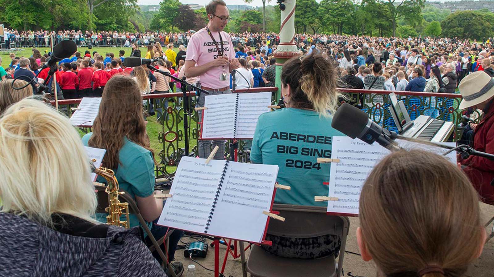 Band members in a gazebo wearing t shirts that say 'Aberdeen Big Sing 2024'
