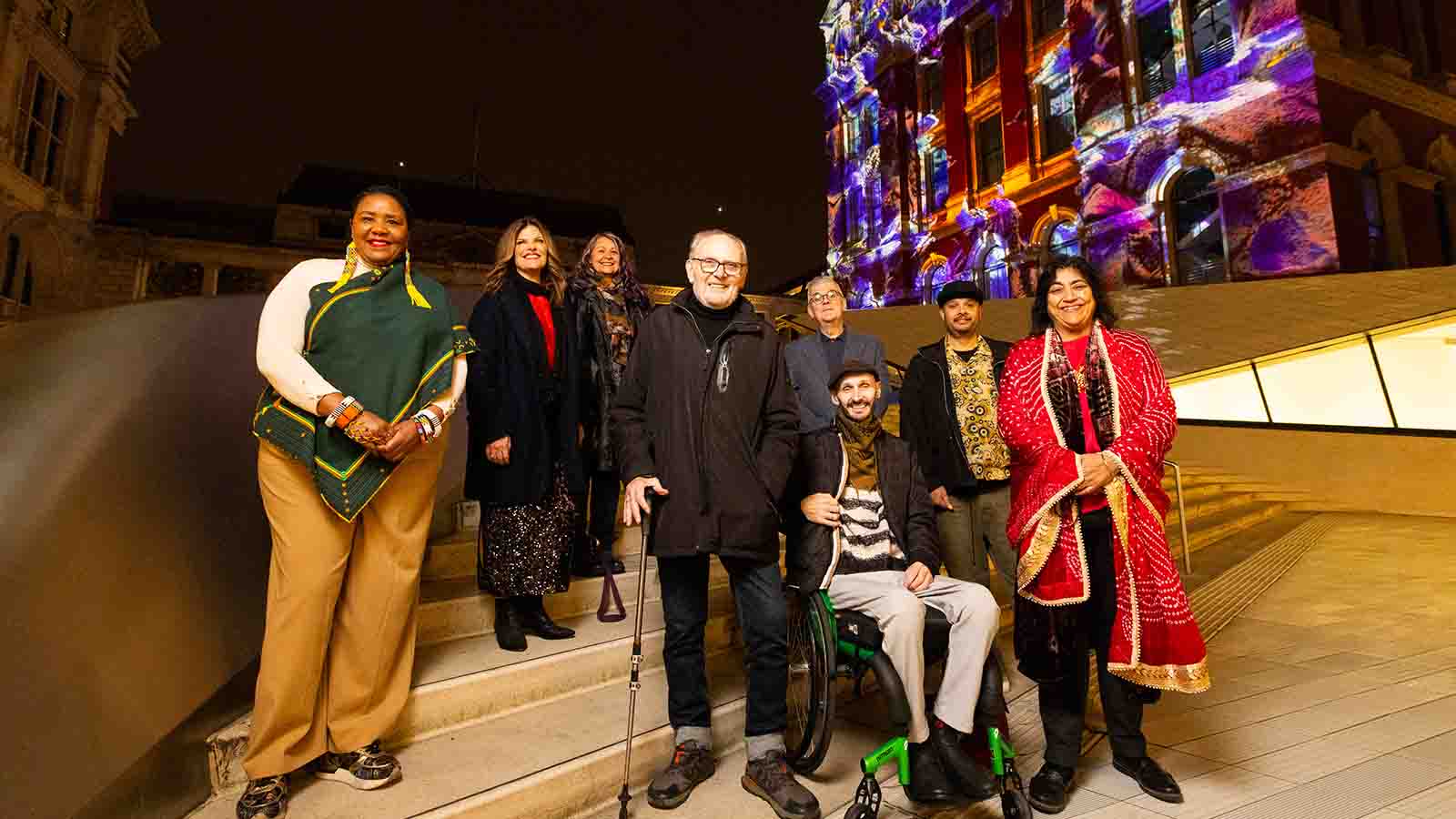 A group of people pictured in front of an old building with a colourful light show projected on to it. These are the seven Game Changers selected to represented arts and film for The National Lottery’s 30th birthday.