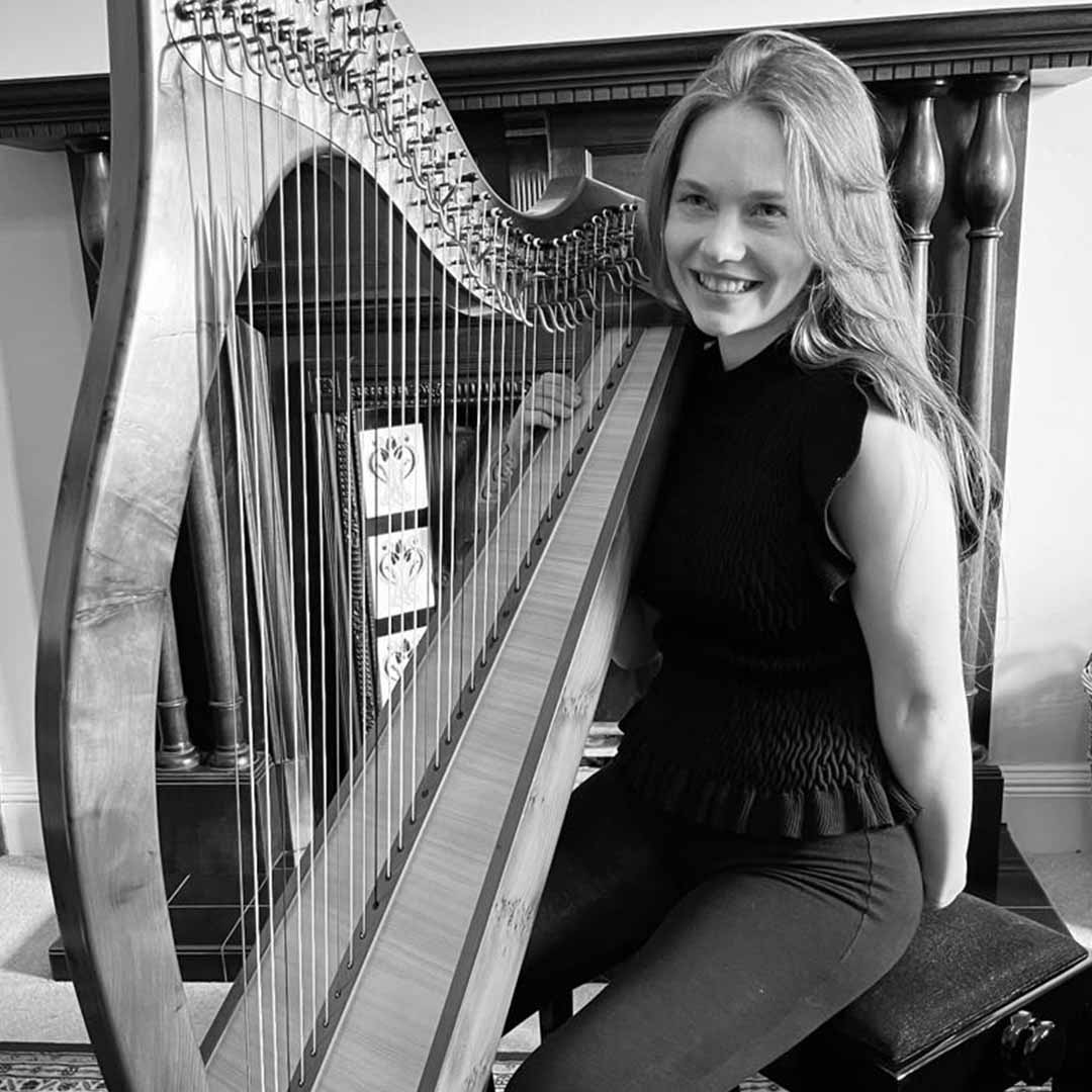 A black and white photo of a woman with long light-coloured hair sitting holding a harp and smiling