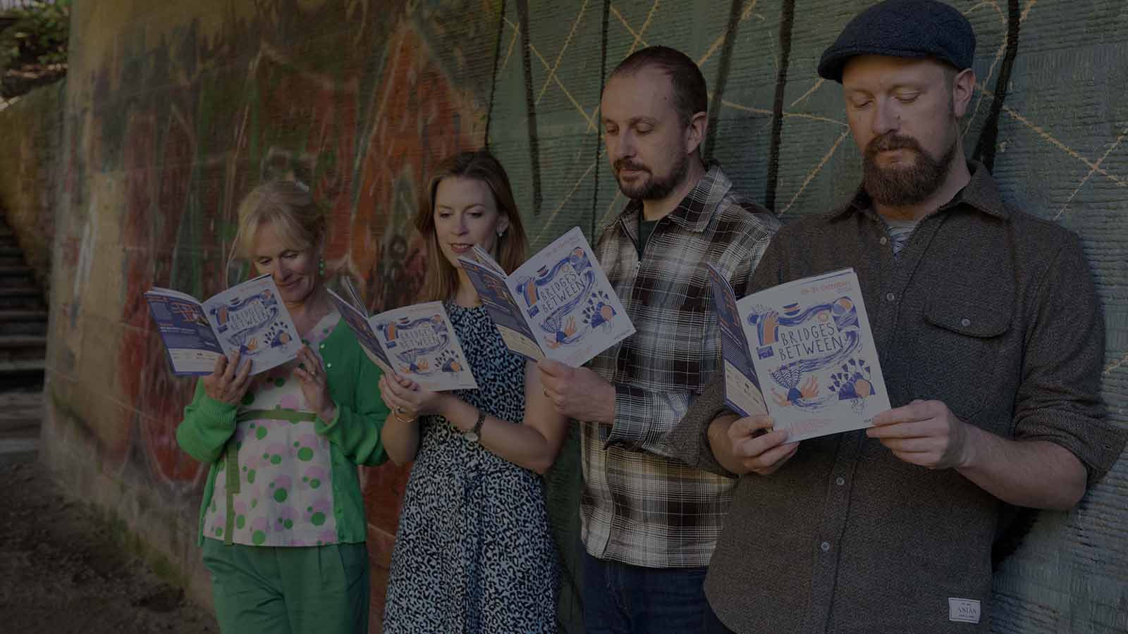 Four people standing together in a line reading a colourful brochure with 'Bridges Between' marked on it.