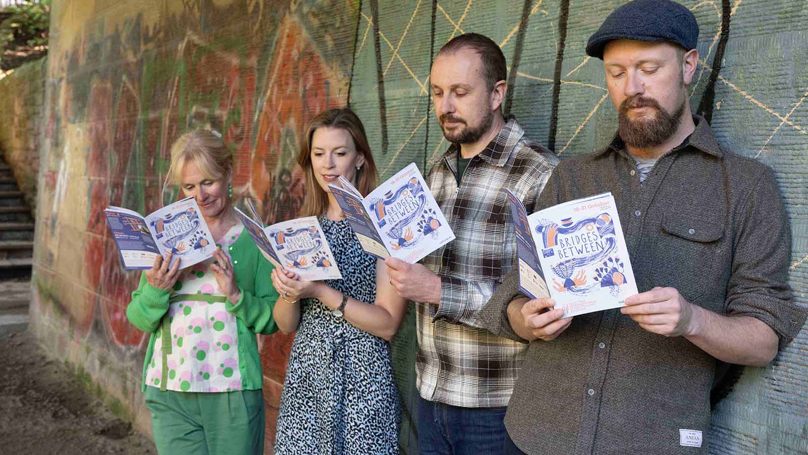 Four people standing together in a line reading a colourful brochure with 'Bridges Between' marked on it.