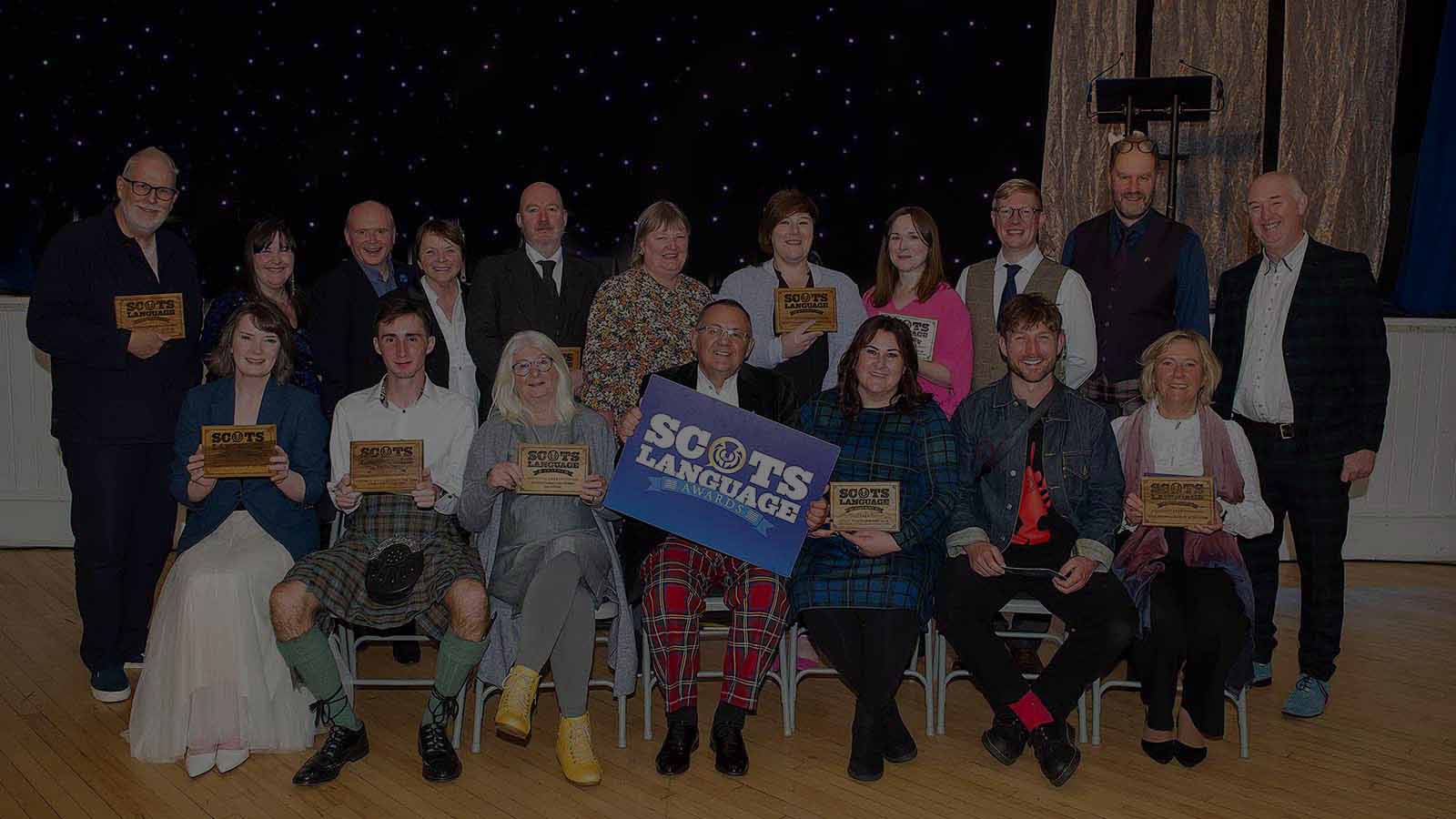 A large group of people, one front row seated, one behind them standing - these are the winners of the 2024 Scots Language Awards.