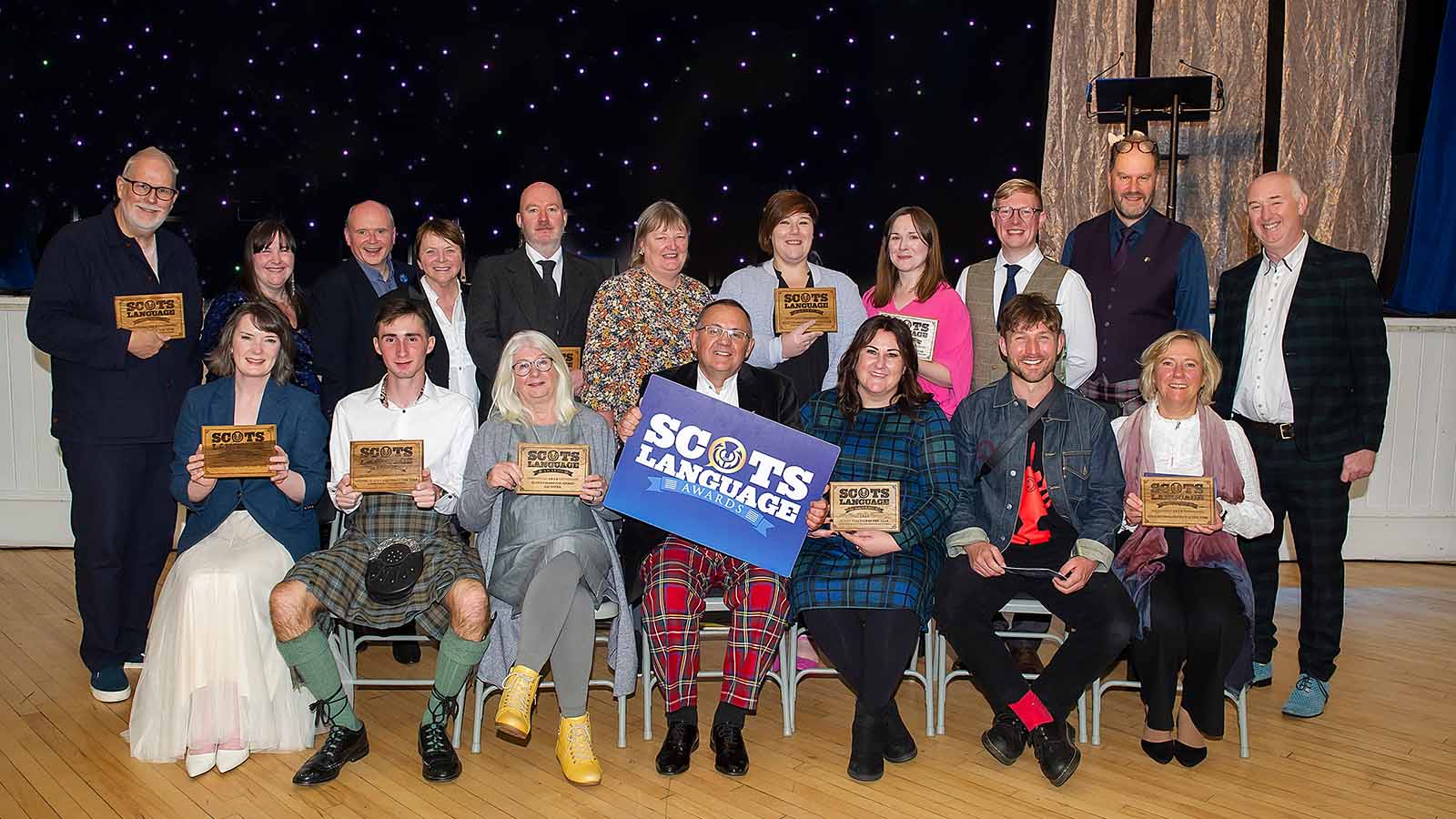 A large group of people, one front row seated, one behind them standing - these are the winners of the 2024 Scots Language Awards.