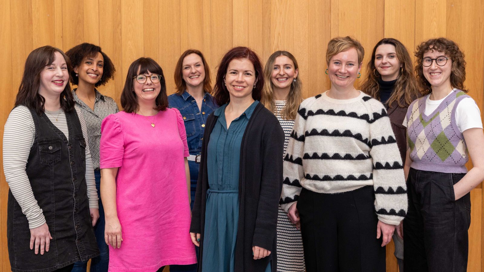 A large group of people standing together in front of a wooden wall, posing for their photo. These are the New Writers Awardees.