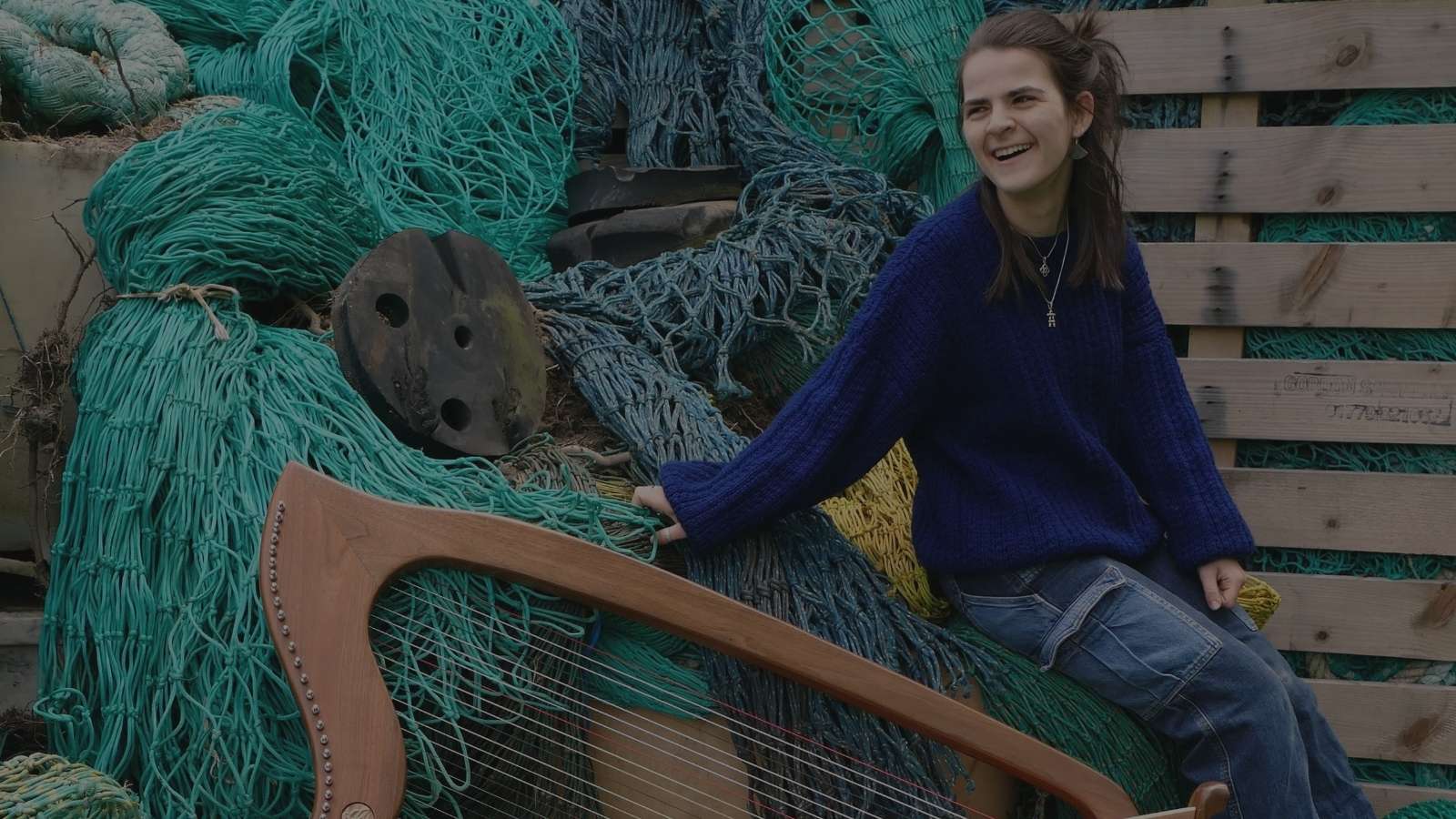 A woman in a bright blue jumper sitting on a pile of colourful fishing nets