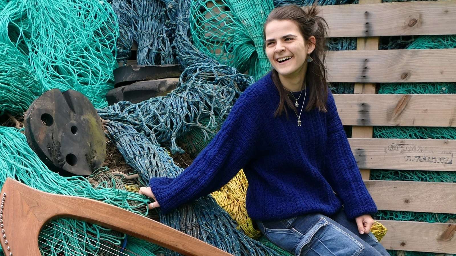 A woman in a bright blue jumper sitting on a pile of colourful fishing nets