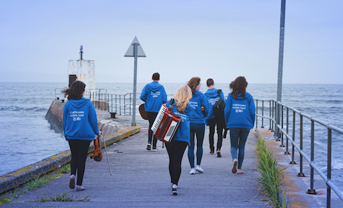 A group of musicians walk along a pier towards the sea